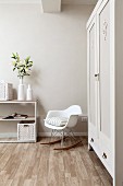 White, designer rocking chair next to painted wardrobe and vase of lilies on top of open-fronted shelving in corner of bedroom