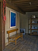 Simple, retro bench on rustic wooden floor in restored interior with wood-beamed ceiling and modern, blue artwork on wall