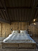 Doppelbett mit weisser Bettwäsche in minimalistischem, holzverkleidetem Schlafzimmer mit rustikalem Flair