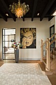 Eingangshalle mit extravaganter Pendelleuchte an Holzdecke, im Hintergrund Marilyn-Monroe-Portrait an Wand, davor Blumenstrauss in Bodenvase
