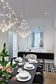 White place settings on black table below designer, LED pendant lamps in dining room