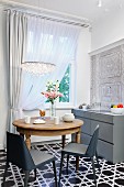 Round wooden table and fifties-style grey chairs on black and white tiled floor with geometric pattern