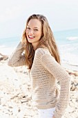 A happy young on a beach wearing a crocheted jumper