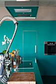 Kitchen island with stainless steel worksurface and professional tap fittings; fitted kitchen appliances in turquoise custom cupboards
