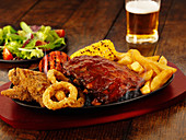 A mixed grill platter featuring chicken, spare ribs, chips and beer