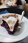A slice of blueberry pie dusted with icing sugar on a plate