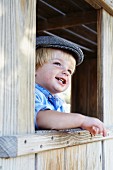 Little boy looking out of window of wooden cabin