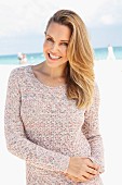 A blonde woman on a beach wearing a long, knitted jumper