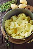 Mashed potatoes with thyme in a copper pot on a wooden surface