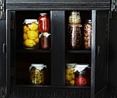Various jars of preserves in a wooden cupboard