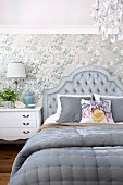 Doppelbett mit gepolstertem Kopfteil grau bezogen, vor tapezierter Wand in elegantem Schlafzimmer