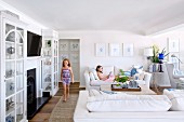 Girl in interior with white sofa set and glass-fronted cabinets against wall