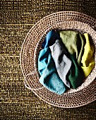 Colourful fabrics in seagrass basket on woven mat and silvery-green structured carpet