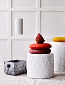 Brightly coloured cushions on stools with diamond structured surfaces and woven basket in front of white-panelled wall