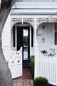 Half-open garden gate outside white 19th-century house with ornate façade