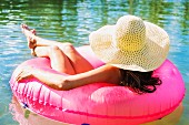 A woman wearing a sunhat sitting in a large, pink rubber ring