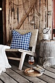 Sessel mit Kissen auf rustikalem Dielenboden vor Holzwand auf Veranda
