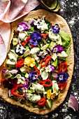 Avocadosalat mit Essblüten, Paprika, roten Zwiebeln und Salatblättern auf blindgebackenem Pizzaboden