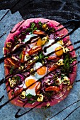 Beetroot pizza dough with broccolini, red onions, tomatoes, goat's cheese, rocket, cheese, fired eggs and balsamic cream