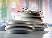 A stack of plates and fabric napkins with cutlery in front of a kitchen window