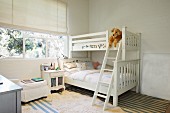 White bunk beds and bedside cabinet below window in children's bedroom