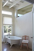 Free-standing, vintage bathtub next to window and below transom window in interior wall