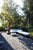 Corner bench with white cushions and fire bowl on sunny, gravel terrace in garden