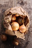 Onions in a paper bag on a wooden surface