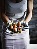Frau hält Tuch mit Stroh und Eiern in beiden Händen