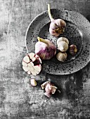 Fresh garlic bulbs and oriental garlic, whole and sliced on and next to a grey plate