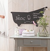 Hand-crafted, bathtub-shaped blackboard on white, wooden bathroom wall
