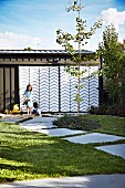 Sandspielplatz mit Kindern vor Garage mit Stahl-Plexiglas-Schiebetür in Zick-Zackmuster und sommerlichem Garten