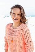 A young woman on a beach wearing an apricot coloured summer jumper