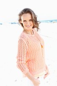 A young woman on a beach wearing an apricot coloured summer jumper