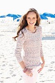 A young, long-haired woman on a beach wearing a knitted jumper