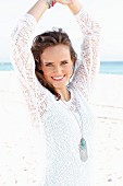 A young, long-haired woman on a beach wearing a white lace dress