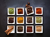 Various spices in square dishes on a chalkboard surface
