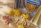 Various types of pasta and a pasta machine on a wooden table