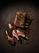 Grilled saddle of lamb on a brown metal surface with herbs and chilli
