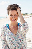 A woman with short, brown hair on a beach wearing a light knitted jumper