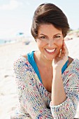 A woman with short, brown hair on a beach wearing a light knitted jumper