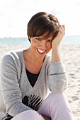 A woman with short brown hair by the sea wearing a grey jumper