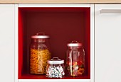 Storage jars in an open, red shelf within a kitchen cupboard