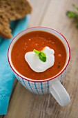Tomato and pepper soup served in a mug with créme fraîche, fresh basil and crusty bread