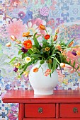Bouquet of multicoloured tulips on red, Oriental chest of drawers against floral wallpaper
