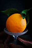 A Seville orange with leaves in a glass bowl