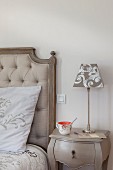 Pale grey bedside table next to bed with button-tufted headboard