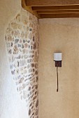 Wrought iron sconce lamp with white lampshade next to stone wall