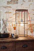 Tischleuchte mit Lampenschirm aus Maschendraht neben Vintage Behältern mit Glashauben
