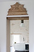 Carved ornament above lintel of interior door with view of free-standing bathtub in country-house ambiance